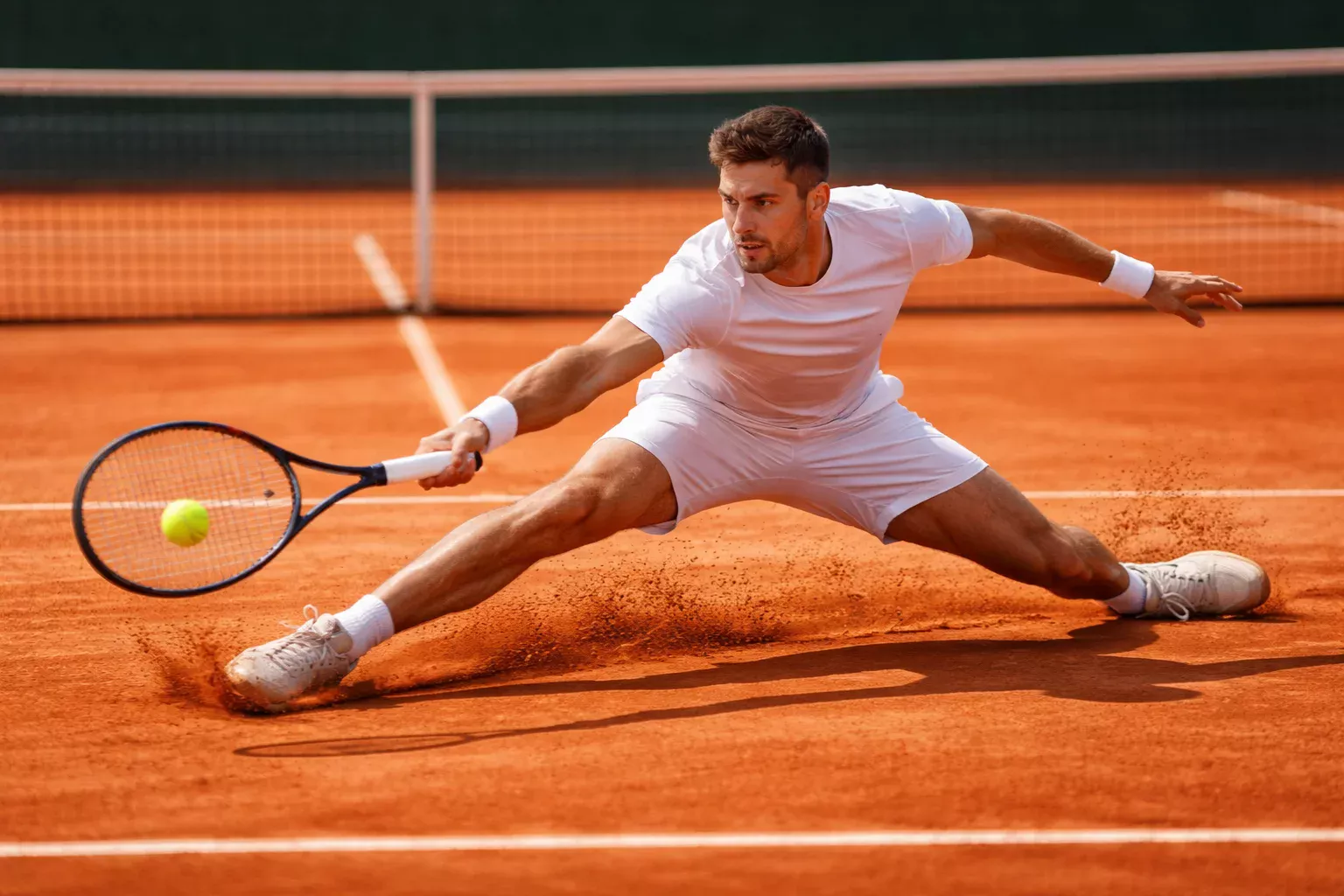 Tenista deslizándose sobre tierra batida para alcanzar una pelota
